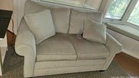 Front view of beige fabric love seat showing cushions and pillows, no stains or tears visible