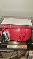 Red Everlast boxing glove signed by George Foreman in a display case with a commemorative plaque.