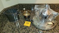 All silver-plated items arranged on kitchen counter including tea server mostly wrapped in plastic.