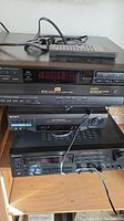 Stack of Sony electronic components including 5-disc CD changer, VHS player, and stereo receiver with remote control on top