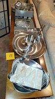 Photo showing an overview of the stainless steel serving items including napkin holder with plastic utensils, round divided tray with central bowl, two oval trays, and other bowls stacked.