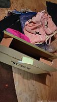 Tumi branded cardboard box partially open with pink backpacks and items inside
