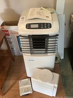 Full front view of the portable Arcticaire air conditioner showing included hoses and attached papers on top.