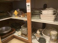 Photo of kitchen cupboard shelf with ceramic roasting dish with lid, mixing bowls, aluminum baking tins, glass bowls, electric heaters, and hand mixers.