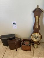 Binoculars in leather cases, vintage compass in wooden box, and wooden wall-mounted barometer with thermometer and hygrometer.