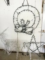 Photo showing large wire circular wreath light display with bow design hanging on wall, with visible wire and string lights.