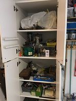 Full view of opened cabinet containing shelves with various items including plastic bags, containers, socket set, small tools, vice, and mitre box.