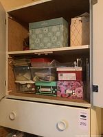 Cupboard interior with decorative boxes and clear plastic containers with craft supplies such as yarn and paints