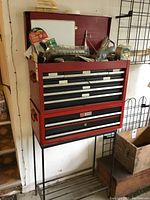Frontal view of red two-piece Craftsman tool chest on black stand with items on top