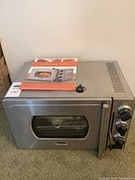 Full view of the stainless steel pressure oven with user manual on top.