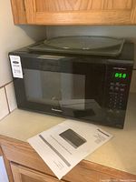 Panasonic black microwave oven on kitchen counter with user manual in front
