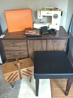 Full view of Pfaff 1199 sewing machine on top of wooden desk with cushioned stool and wooden sewing box in front. Accessories visible on desk.