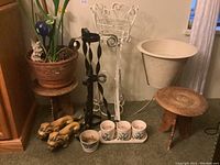 Full view showing plant stands and planters including white metal stand, black twisted metal stand, ceramic planter, wooden stands, and dog figurines.