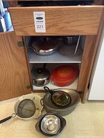Cabinet with various pots, strainers, roaster, small pans inside and on floor
