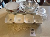 Full view of all items including Pyrex bowls, clear glass bowl, ceramic holiday serving dish, and doilies on countertop.