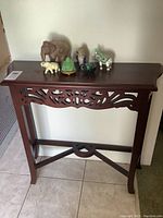Front view of wood side table with six elephant and decor figurines arranged on top.