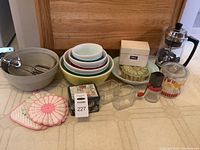Full view of all items in the lot including bowls, canisters, tin, coffee percolator, pot holders, and mixing bowl with mixer