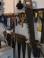 Wide view of workbench wall showing vintage hand saws, hammers, clamp, and hanging trouble light