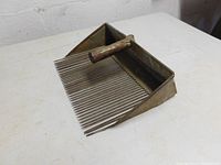 Side angle view of antique cranberry scoop showing metal tines and wooden handle.