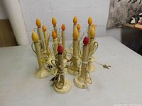Fourteen vintage electric Christmas window candles grouped on a table showing various flame bulb colors and some with octagonal and ribbed round bases.