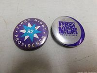 Front view of two circular pins: left pin dated 1992 with star design, right pin with purple text on silver background
