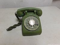 Front angle view of vintage green rotary dial telephone showing handset, dial plate, and coiled cord.