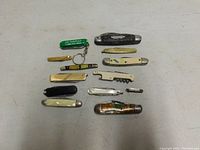 Top-down view of all 12 vintage pocket tools arranged on a flat surface, showing variety in size, handle material, and tool types.