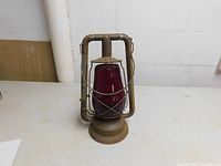 Front view of antique Dietz railroad lantern with ruby red glass and rusted metal frame.