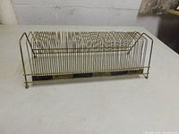 Side view of the vintage metal 45 RPM record holder showing its rectangular wire frame structure with closely spaced slots for holding records upright.