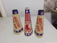 Three vintage Boston Red Sox popcorn megaphone cones arranged upright on a table, showing front and side views of the cones with team branding