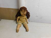 Full view of the 19-inch doll sitting with visible porcelain arms and legs, cloth body, and yarn hair.