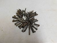 Top down view of 35 metal skeleton keys grouped in a cluster on a white surface showing various key bit designs and hollow barrels.