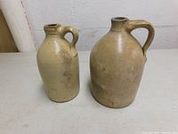 Two antique earthenware jugs standing side by side, clearly showing size difference and handles