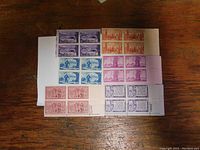 Nine sheets of uncancelled U.S. stamps laid out on a wooden surface, each sheet containing multiple stamps in blocks of four or more with margin markings.