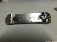 Close-up photo of a vintage metal bottle opener engraved 'Knickerbocker Beer' showing the flat bent design for prying bottle caps.