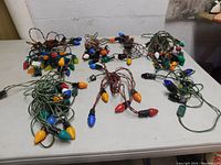 Eight vintage Christmas light strings displayed unordered on a table showing multi-colored bulbs and varied wiring