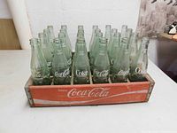 Front view of vintage red wooden Coca-Cola case holding 24 empty glass bottles with white Coca-Cola text on sides.