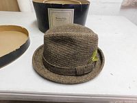 Brown herringbone wool men's hat with short brim and fabric bow band, displayed next to vintage hat box with label.