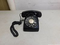 Full view of the vintage black Western Electric rotary dial telephone with handset and coiled cord on a light surface.