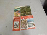 Six vintage road maps displayed on a table, showing colorful illustrated covers for Rhode Island, Northeast, Ohio, and Pittsburgh, Pennsylvania maps.