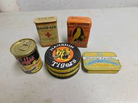 Overview photo of all five vintage tins together including Band-Aid, Hartz Mountain bird food, Mickey's coffee, Allenbury's Pastilles, and Hanshin Tigers tins.