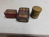 Three vintage tins arranged: Jack Daniels whiskey tin, Oriental dragon tin, and Gofkauf's Auto Store tin with bulbs inside