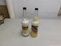 Full view of two unopened vintage Wildroot Cream Oil bottles with black caps, showing original labels and thick cream oil content inside bottles.