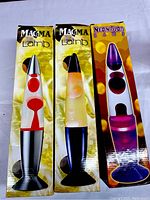 Three boxed lava lamps displayed vertically showing front packaging with brand names Magma and Neon Blob and lava lamp images.