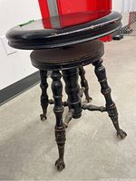 Photo showing the full antique piano stool with black painted round seat and ornate turned legs.