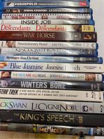 Photo shows a close-up view of 20 Blu-Ray movie cases stacked, titles visible including Persepolis, Animal Kingdom, The Trotsky, Inside Job, Descendants, War Horse, Revolutionary Road, Kingdom of Heaven, Stranger than Fiction, Blue Jasmine, The Kids Are All Right, Winter's Bone, Black Swan, The King's Speech, Micmacs.
