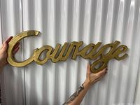 Metal word art 'Courage' held in hands showing size and discoloration on the letter C.
