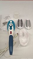 MiAmora handheld garment steamer with attachments including two brush heads, measuring cup, protective glove, and user manual on white background.
