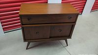 Front view of mid century modern wood cabinet showing hidden drawer and sliding doors with cutout handles and tapered legs