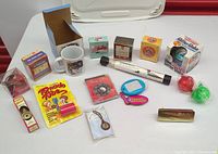 Overall photo showing assortment of novelty items including toys, facial kit, book, glitter globe, tornado tube, sundial necklace, pocket scribbler, and cat mug.